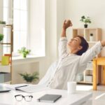 A professional taking a quick stretch break at their desk, smiling with renewed energy amid office plants.