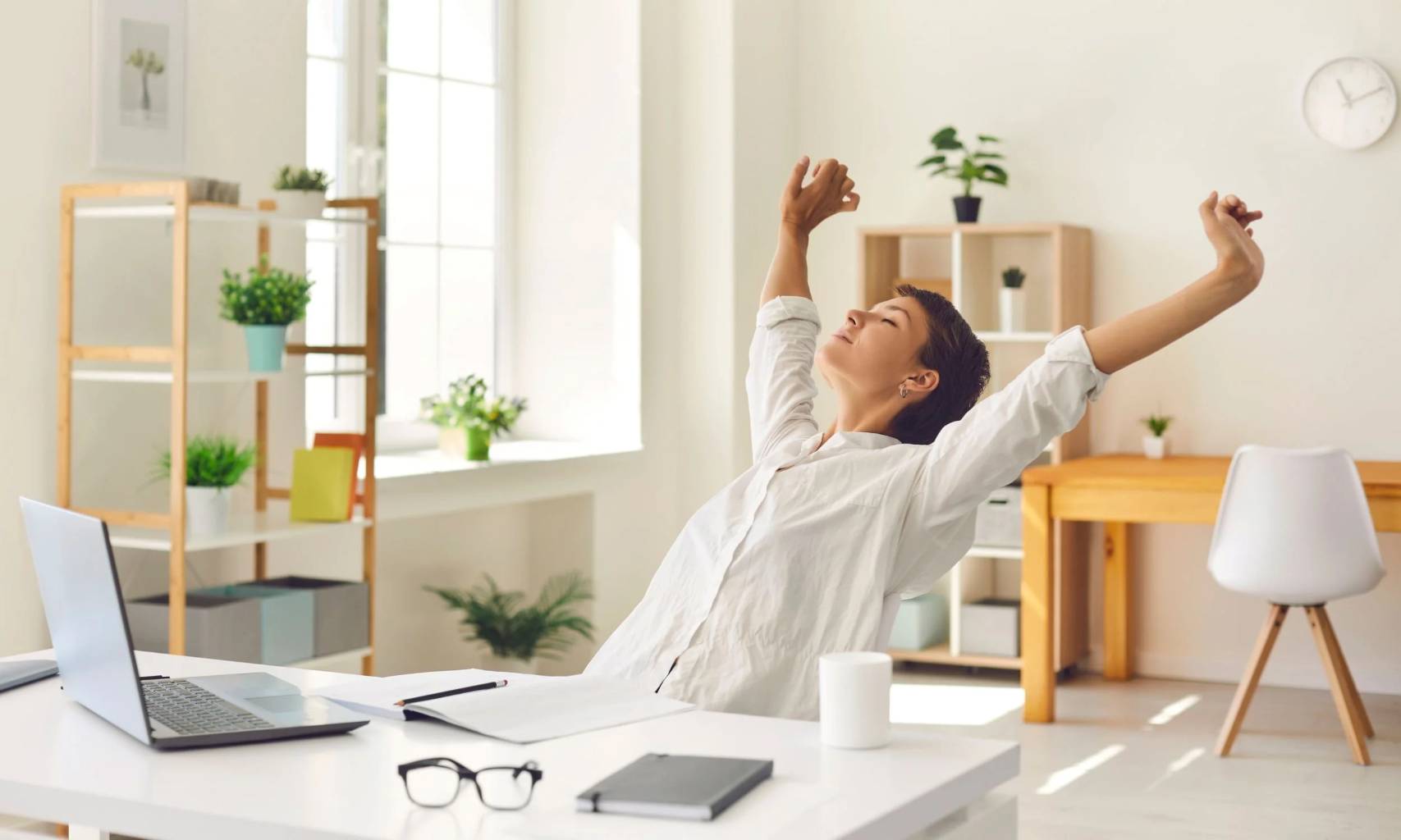 A professional taking a quick stretch break at their desk, smiling with renewed energy amid office plants.